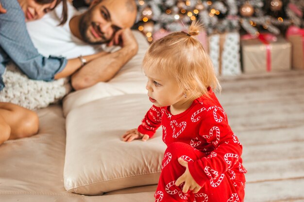 Een klein meisje in rode pyjama bij gelukkige ouders op de bank voor Kerstmis