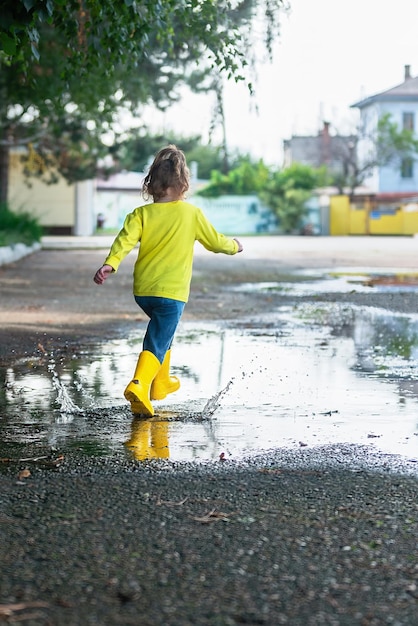 Een klein meisje in rubberen gele laarzen rent vrolijk door de plassen tijdens een wandeling