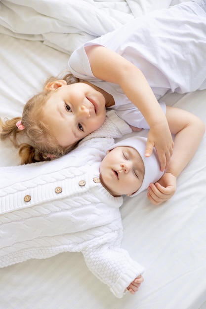 Een klein meisje knuffelt een slapende pasgeboren zus of broer op een wit bed thuis twee kinderen in het gezin