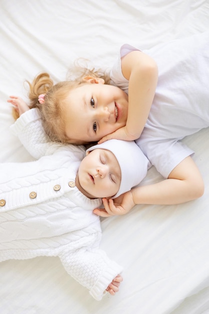 een klein meisje knuffelt een slapende pasgeboren zus of broer op een wit bed thuis twee kinderen in het gezin