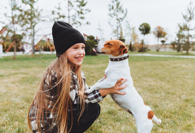 Een klein meisje kust en knuffelt haar Jack Russell-terriërhond in het park Liefde tussen de eigenaar en de hond een kind houdt een hond in zijn armen