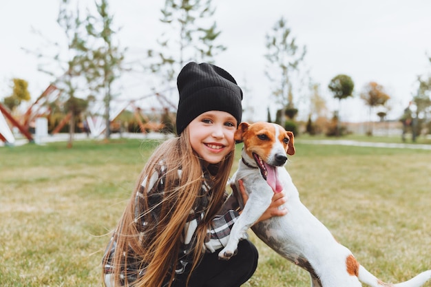 Een klein meisje kust en knuffelt haar Jack Russell-terriërhond in het park Liefde tussen de eigenaar en de hond een kind houdt een hond in zijn armen