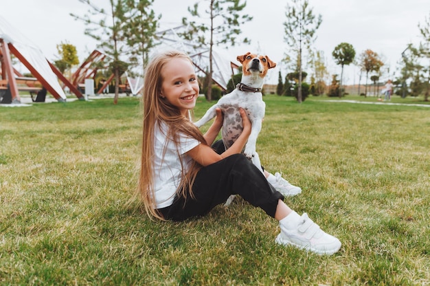 Een klein meisje kust en knuffelt haar Jack Russell-terriërhond in het park Liefde tussen de eigenaar en de hond een kind houdt een hond in zijn armen