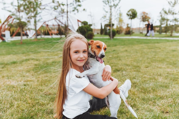 Een klein meisje kust en knuffelt haar Jack Russell-terriërhond in het park Liefde tussen de eigenaar en de hond een kind houdt een hond in zijn armen