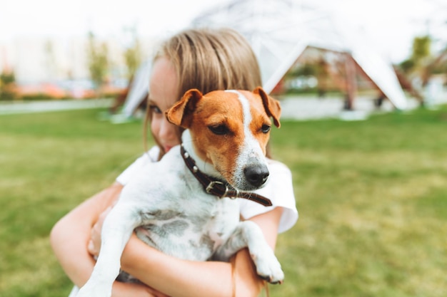 Een klein meisje kust en knuffelt haar Jack Russell-terriërhond in het park Liefde tussen de eigenaar en de hond een kind houdt een hond in zijn armen