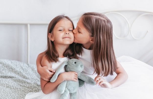 Een klein meisje kust haar zusje op de wang. Meisjes rusten in de kinderkamer