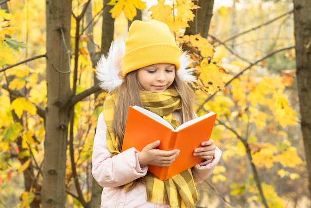 Een klein meisje leest een boek in het bos in de herfst.