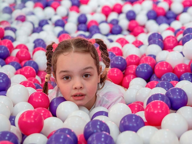 Een klein meisje leunt uit kleurrijke plastic ballen in een groot droog zwembad.