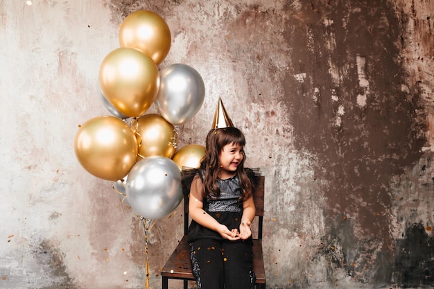 Een klein meisje met ballonnen het kind viert zijn verjaardag de baby zit op een stoel naast ballonnen