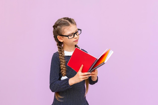 Een klein meisje met een bril houdt schoolboeken in haar handen en glimlacht breed op een roze geïsoleerde achtergrond Educatieve cursussen voor schoolkinderen