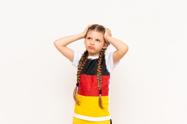 Een klein meisje met een Duitse vlag op een T-shirt met lang haar gevlochten in staartjes en haar gulova geklemd met twee handen op een witte geïsoleerde achtergrond