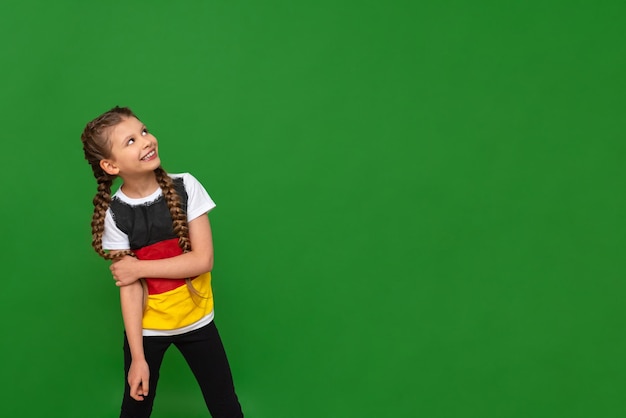 Een klein meisje met een Duitse vlag op haar T-shirt kijkt naar uw advertentie op een groene geïsoleerde achtergrond Duitse taalcursussen voor schoolkinderen Ruimte kopiëren