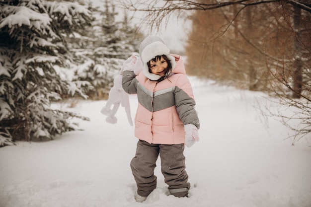 Een klein meisje met een gebreide haas staat op straat onder de vliegende sneeuw. winter dag
