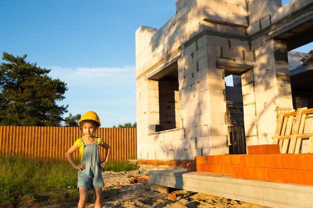 Een klein meisje met een gele veiligheidshelm speelt bouwer op de bouwplaats van haar toekomstige huis. Dromen van verhuizen, een beroep kiezen, onderwijs voor kinderen.