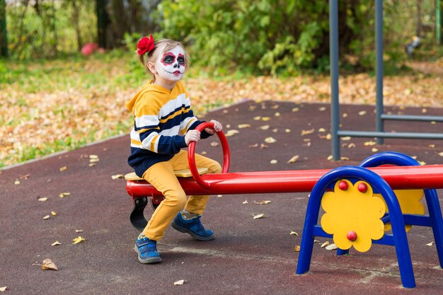 Een klein meisje met een geverfd gezicht, glimlachend op de speelplaats, viert Halloween of Mexicaanse dag van de doden ...