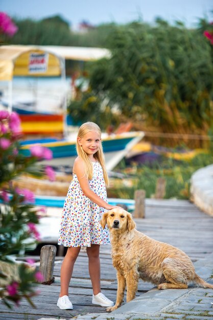 Een klein meisje met een hond aan de kade bij de rivier in een witte zomerjurk in de stad Dalyan. Kalkoen.