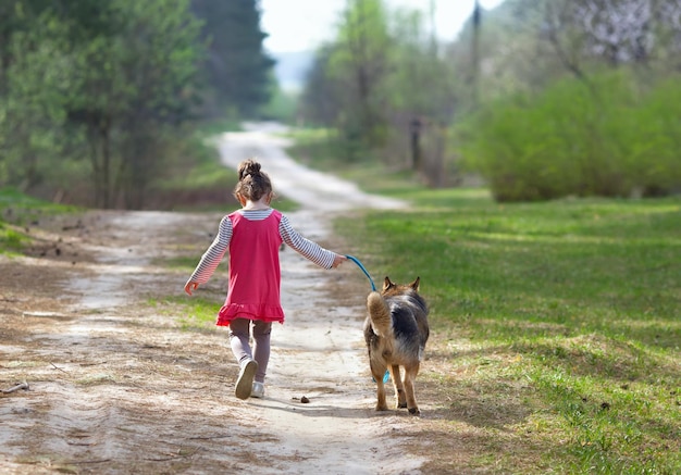 Een klein meisje met een hond loopt langs de onverharde weg op het platteland