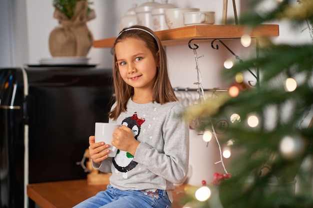 Een klein meisje met een kop hete thee droomt van een kerstcadeautje.