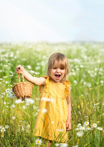 Foto een klein meisje met een open mond en een mand in haar handen loopt over het veld met madeliefjes
