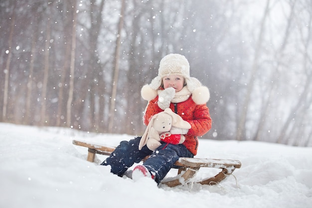 een klein meisje met een pluizige hoed loopt op een besneeuwde winterdag