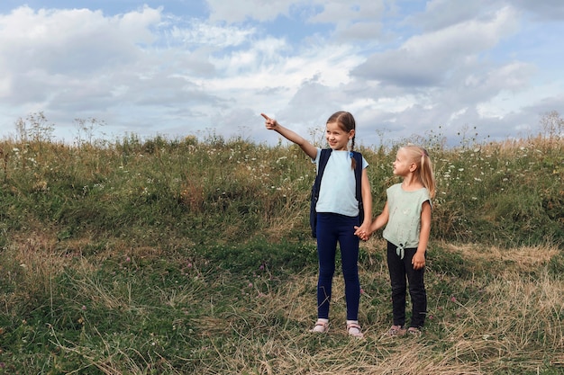 Een klein meisje met een rugzak op haar schouders wijst de weg naar haar zus