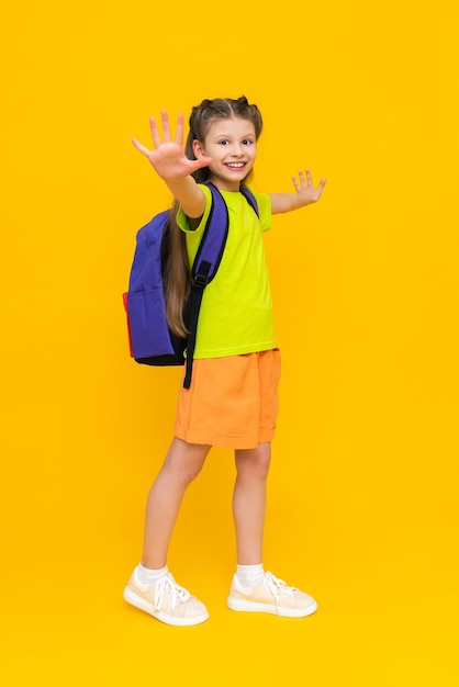 Een klein meisje met een schoolrugzak Een kind in zomerbroek gaat naar onderwijscursussen Een gelukkig kind met een schooltas Een schoolmeisje van volledige lengte op een gele geïsoleerde achtergrond