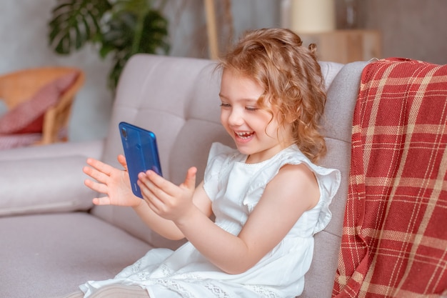 Een klein meisje met een telefoon zit op de bank