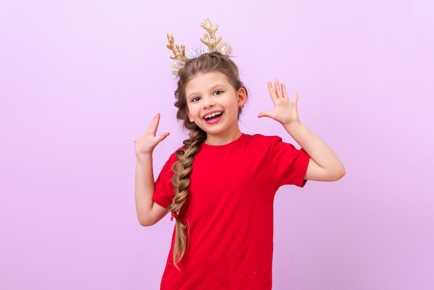 Een klein meisje met feestelijke nieuwjaarshoorns op haar hoofd is erg blij en laat haar handpalmen zien. Op een paarse geïsoleerde achtergrond.