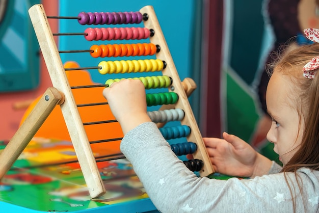 een klein meisje met lang haar rekent op een felgekleurd telraam in een kinderspeelkamer