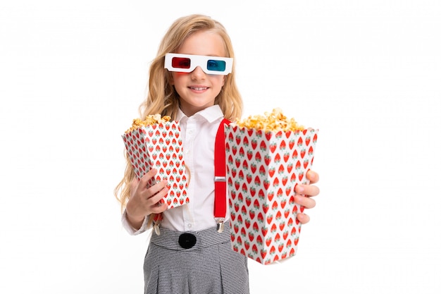 Een klein meisje met make-up en lang blond haar met pop-corn en 3D-bril en glimlach