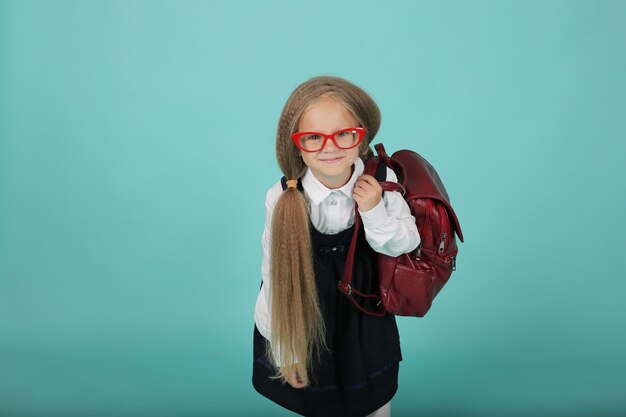 Een klein meisje met paardenstaarten in een wit overhemd en een grijze zomerjurk een schoolmeisje met een rugzak