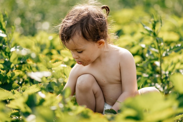 Een klein meisje met rijp op haar gezicht proeft een zoete aardbeipijl in de dorpstuin