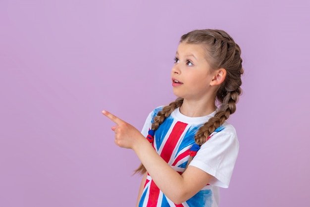 Een klein meisje met staartjes en een afbeelding van de engelse vlag op een t-shirt wijst met haar vinger opzij.