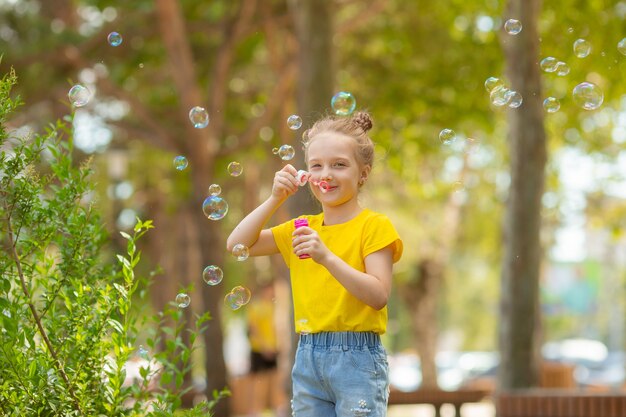 Een klein meisje met zonnebril blaast zeepbellen in het park in de zomer