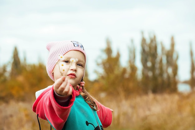 een klein meisje op een herfstwandeling houdt een kleine wilde bloem in haar hand