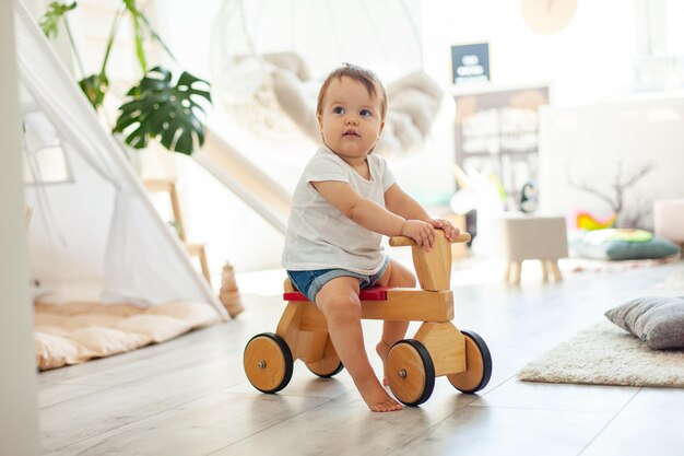 Een klein meisje op een houten scooter in de kinderkamer.