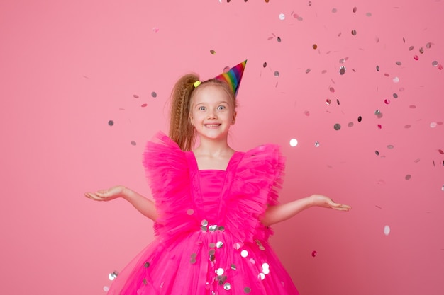 Een klein meisje op een roze achtergrond vangt confetti en viert haar verjaardag