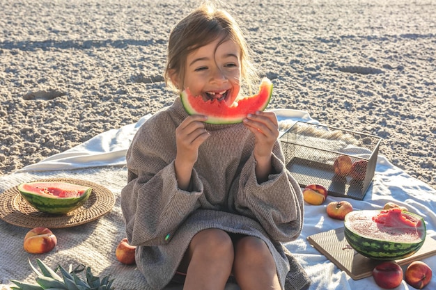 Een klein meisje op een zandstrand aan zee eet een watermeloen