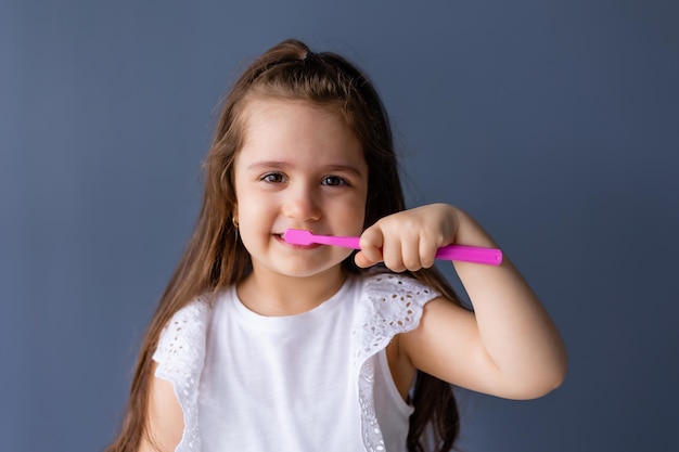 Een klein meisje poetst haar tanden met een roze tandenborstel.