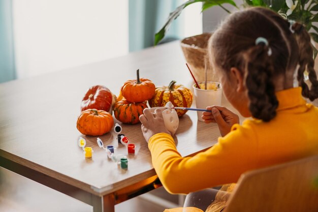 Een klein meisje schildert een met de hand gemaakte pompoen van klei Halloween-feest Knutselen voor kinderen