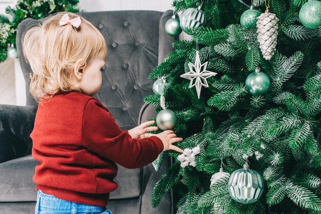 Een klein meisje siert een kerstboom