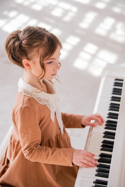 Een klein meisje speelt een grote witte piano in een heldere, zonnige kamer