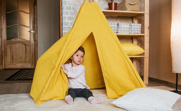 Een klein meisje speelt in een gele tipi