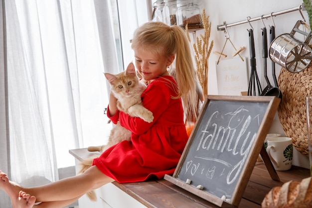 Een klein meisje speelt met een kitten in de keuken van het huis. Het concept van een menselijke familie en een huisdier