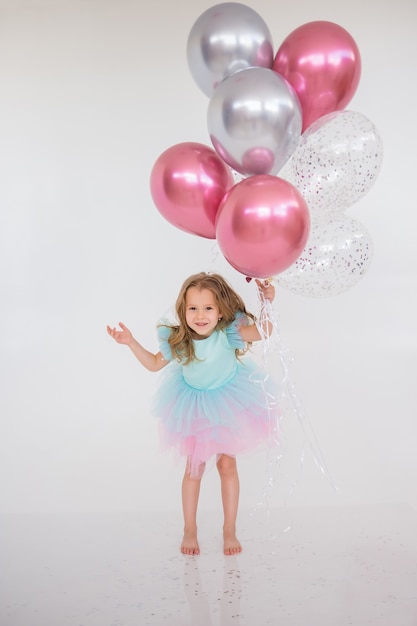 Een klein meisje springt met een bos ballonnen op een witte achtergrond met een plek voor tekst. vakantie verjaardag