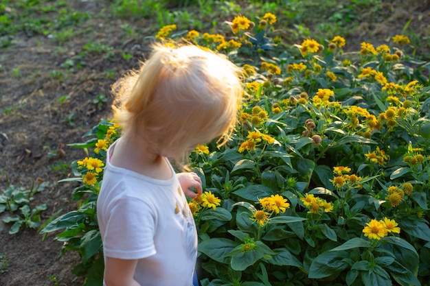Een klein meisje staat bij een bloembed met gele bloemen Vakantie met kinderen op het platteland