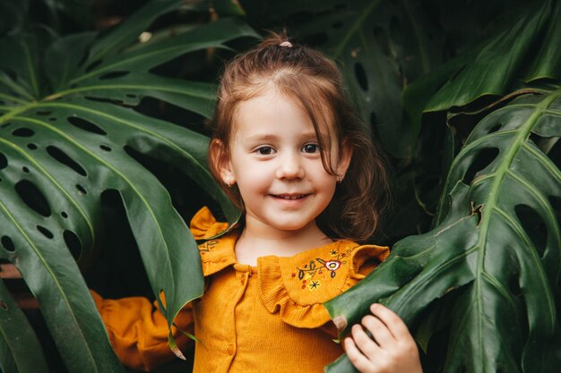 Een klein meisje staat in een botanische tuin omringd door monstera