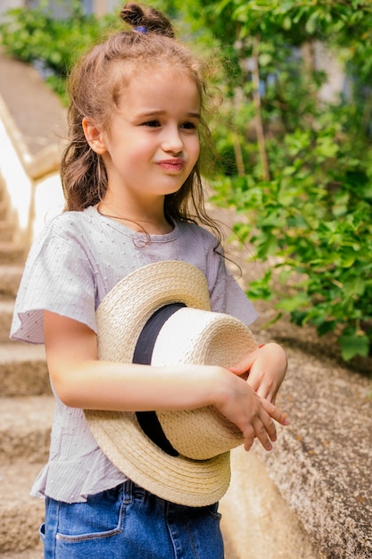 Een klein meisje staat in het park en houdt een hoed in haar handen. Het kind is blij en lacht.