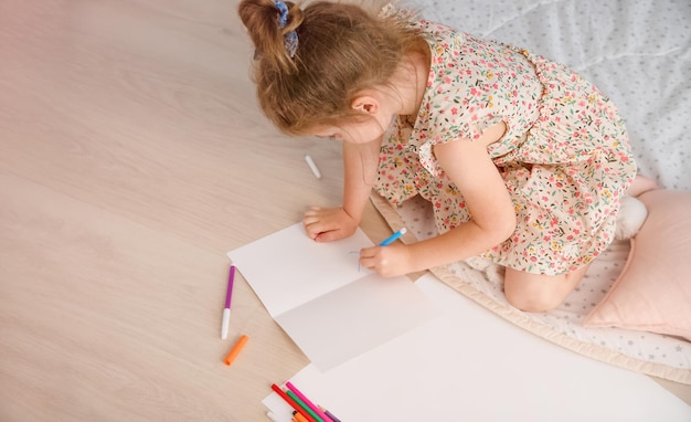 Een klein meisje tekent in de kamer op de vloer Kopieer ruimtemodel