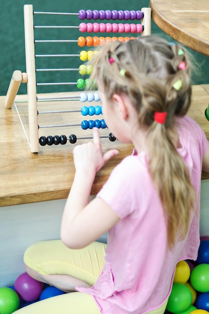 Een klein meisje telt met haar vinger op een gekleurd houten telraam dat met haar rug naar de camera zit